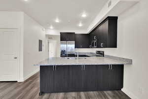 Kitchen with a peninsula, dark cabinetry, light stone countertops, appliances with stainless steel finishes, and dark wood-type flooring