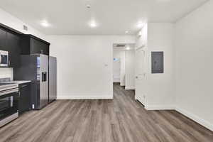 Kitchen featuring dark cabinets, appliances with stainless steel finishes, electric panel, light wood-style flooring, and light stone countertops