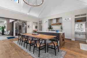 Dining area featuring high vaulted ceiling, light wood-style flooring, a barn door, and a notable chandelier