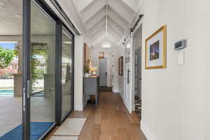 Hall with baseboards, a barn door, vaulted ceiling, and hardwood / wood-style flooring