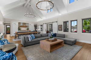 Living room featuring beamed ceiling, light wood-style floors, high vaulted ceiling, a barn door, and a chandelier