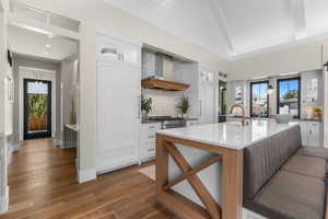 Kitchen with backsplash, white cabinets, a healthy amount of sunlight, and wall chimney exhaust hood