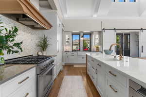 Kitchen featuring high end stove, light wood-type flooring, a barn door, a sink, and custom exhaust hood
