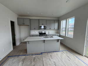 Kitchen with a sink, gray cabinets, baseboards, light countertops, and appliances with stainless steel finishes