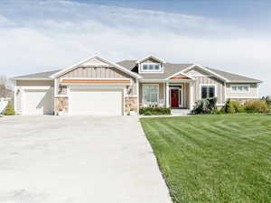 Craftsman-style home with board and batten siding, driveway, a front yard, an attached garage, and stone siding