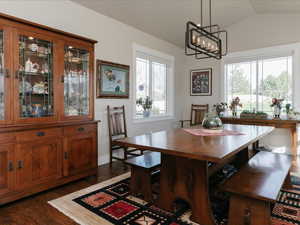 Dining area with an inviting chandelier, dark wood-style floors, and lofted ceiling