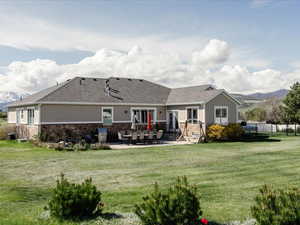 Rear view of house with fence, a yard, a patio area, and stone siding