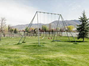 View of playground with a lawn, a rural view, fence, and a mountain view