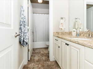 Bathroom featuring toilet, stone finish flooring, shower / bath combination with curtain, and vanity