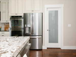 Kitchen featuring baseboards, dark wood finished floors, light stone countertops, and stainless steel appliances
