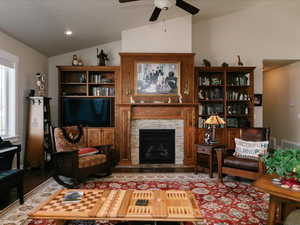 Sitting room featuring wood finished floors, a ceiling fan, lofted ceiling, and a stone fireplace