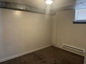 Empty room featuring visible vents, dark carpet, and a baseboard radiator