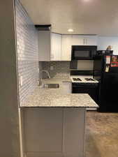 Kitchen with light stone countertops, a sink, black appliances, a peninsula, and white cabinetry