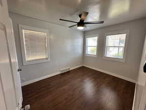 Empty room featuring dark wood-style flooring, baseboards, and visible vents