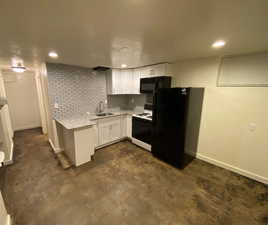 Kitchen with white cabinets, light stone counters, a sink, baseboards, and black appliances