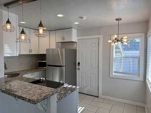 Kitchen with white cabinets, a sink, dark stone countertops, stainless steel appliances, and light tile patterned floors
