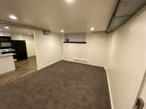 Finished below grade area featuring freestanding refrigerator, recessed lighting, baseboards, and a baseboard radiator