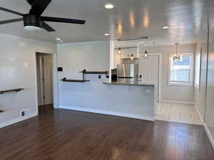 Kitchen with visible vents, baseboards, freestanding refrigerator, ceiling fan with notable chandelier, and dark stone counters