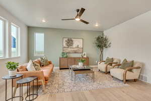 Living room with a ceiling fan, baseboards, light wood-style floors, and visible vents