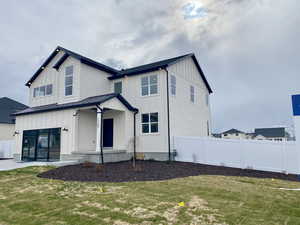 Modern farmhouse with a front lawn, a standing seam roof, fence, and board and batten siding