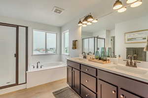 Primary Bathroom featuring double vanity, a sink, a garden tub, and a stall shower