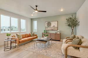 Living room with large windows, recessed lighting, hardwood laminate floors, and a ceiling fan