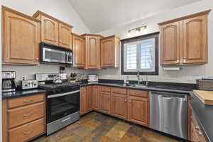 Kitchen featuring a sink, appliances with stainless steel finishes, vaulted ceiling, and dark countertops