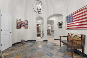 Hallway with stone tile floors, baseboards, a high ceiling, a chandelier, and arched walkways