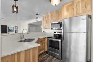 Kitchen with a sink, light countertops, light brown cabinets, stainless steel appliances, and dark wood-type flooring
