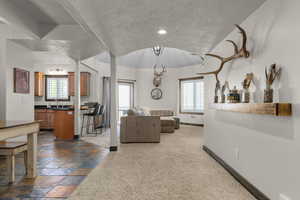 Living area with a textured ceiling, baseboards, lofted ceiling, recessed lighting, and stone tile floors