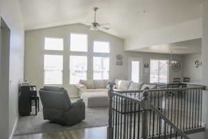 Living room with wood finished floors, ceiling fan, a chandelier, vaulted ceiling, and baseboards