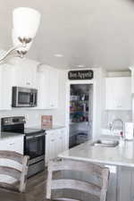 Kitchen featuring appliances with stainless steel finishes, a sink, white cabinetry, and light stone countertops