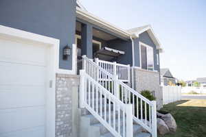 Doorway to property with a garage, brick siding, a porch, and stucco siding