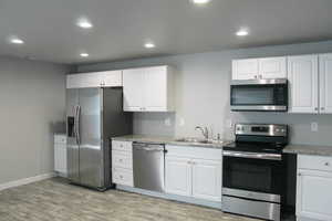 Kitchen featuring stainless steel appliances, a sink, white cabinetry, light wood-style floors, and recessed lighting