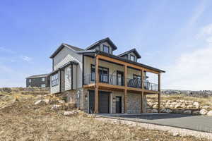 Back of property featuring board and batten siding, a balcony, stone siding, and a garage