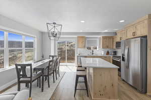 Kitchen with light brown cabinetry, light wood-style floors, a chandelier, a sink, and appliances with stainless steel finishes