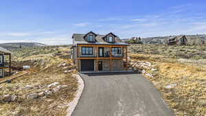 Chalet / cabin with a standing seam roof, driveway, a garage, a balcony, and stone siding