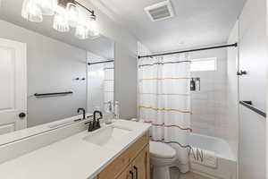 Full bathroom featuring a textured ceiling, visible vents, shower / tub combo, vanity, and toilet