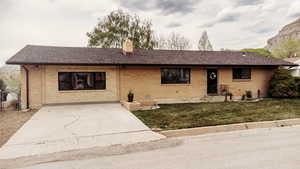 Ranch-style house with brick siding, a chimney, a front yard, and roof with shingles