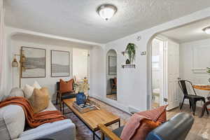 Living area with wood finished floors, a textured ceiling, arched walkways, baseboards, and visible vents