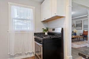 Kitchen featuring dark countertops, dark wood-style floors, white cabinetry, and stainless steel gas range oven