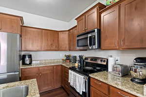 Kitchen with light stone countertops, dark wood-style flooring, appliances with stainless steel finishes, and brown cabinets