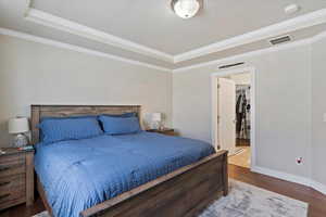 Bedroom with visible vents, a raised ceiling, ornamental molding, and wood finished floors