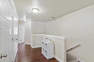 Hallway with baseboards, a textured ceiling, an upstairs landing, and dark wood-style flooring