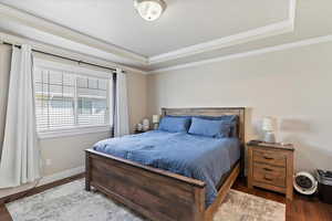 Bedroom with a tray ceiling, crown molding, visible vents, baseboards, and wood finished floors