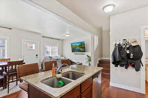 Kitchen featuring a sink, open floor plan, light stone countertops, dishwasher, and dark wood-type flooring