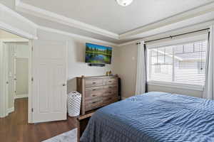 Bedroom featuring a raised ceiling, wood finished floors, and crown molding