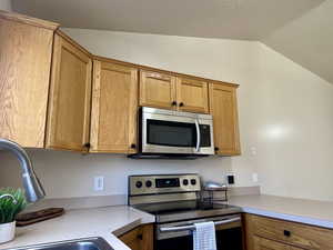 Kitchen featuring brown cabinetry, appliances with stainless steel finishes, vaulted ceiling, a sink, and light countertops