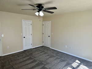 Spare room with dark carpet, a ceiling fan, a textured ceiling, and baseboards