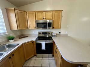 Kitchen featuring light countertops, appliances with stainless steel finishes, a peninsula, and lofted ceiling